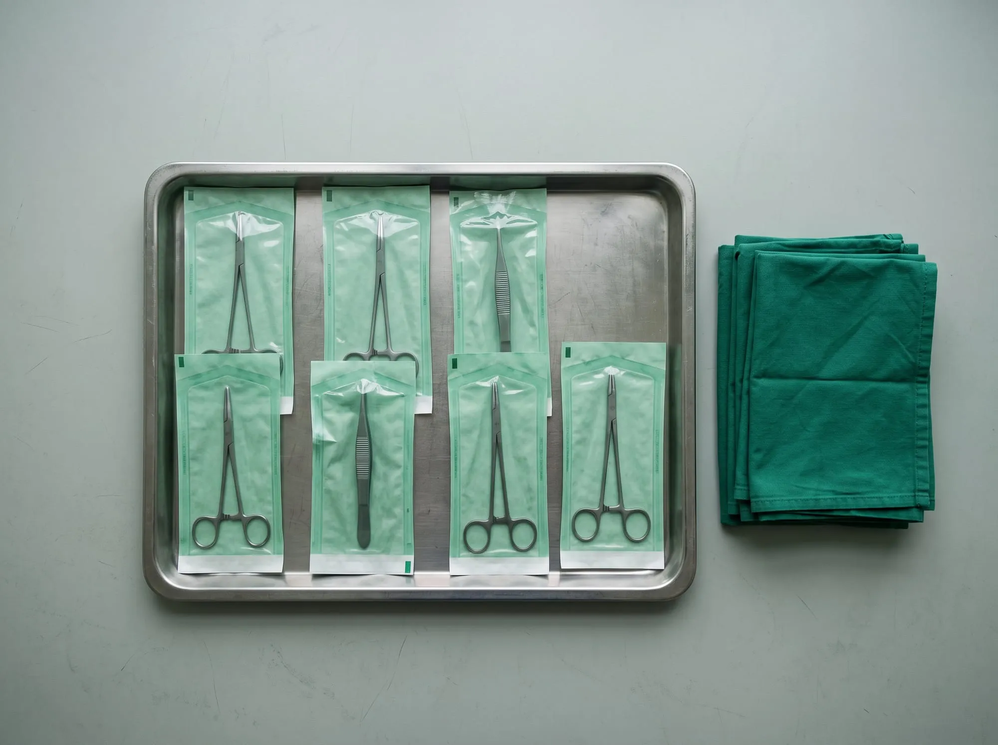 Çelik tepside yeşil sterilizasyon poşetleri içinde cerrahi aletler ve yanında katlanmış yeşil ameliyat örtüleri